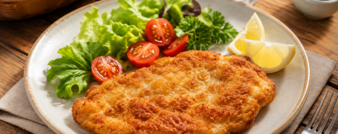 Куриная отбивная на фарфоровой тарелке с салатом овощами и специями на деревянном столе